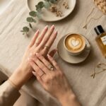Classy modern French tip nails manicure with linen runner, gold jewelry rings, and latte cup flat lay