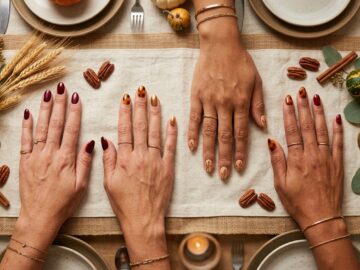 Elegant Thanksgiving nail art manicure flat lay with cozy knit sweater, wine goblet, and autumn tablescape