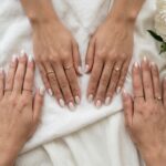 Milky white nails clean girl aesthetic manicure with gold rings, silk linen, and minimalist coffee cup flat lay