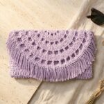 Lavender recycled cotton crochet clutch bag pattern with semi-circle lacy flap and fringe on travertine stone