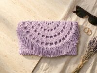 Lavender recycled cotton crochet clutch bag pattern with semi-circle lacy flap and fringe on travertine stone