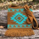 Southwest tapestry crochet crossbody bag pattern with turquoise diamond motif and golden brown fringe on rustic log