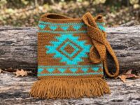 Southwest tapestry crochet crossbody bag pattern with turquoise diamond motif and golden brown fringe on rustic log