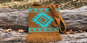Southwest tapestry crochet crossbody bag pattern with turquoise diamond motif and golden brown fringe on rustic log