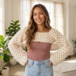 Woman in a sunlit loft wearing a cream fluffy granny stitch crochet shrug bolero over a mauve ribbed tank top