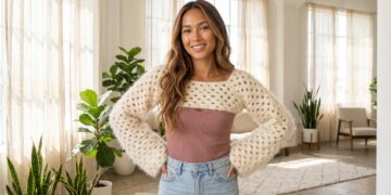 Woman in a sunlit loft wearing a cream fluffy granny stitch crochet shrug bolero over a mauve ribbed tank top