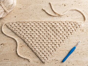 Free crochet bandana pattern hero flat-lay with cream cotton yarn skein and blue 4.0 mm crochet hook