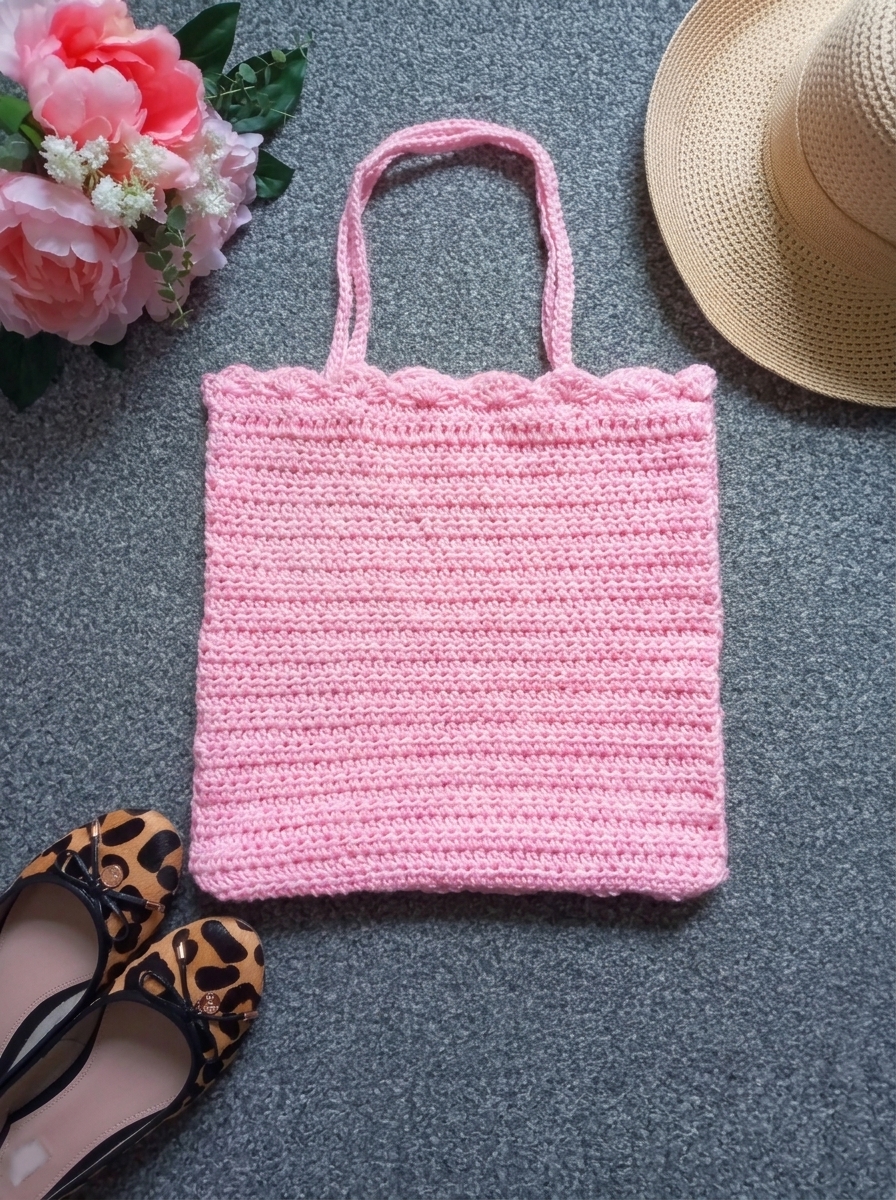 Overhead flatlay of the finished light pink crochet tote bag pattern styled with a straw sun hat and pink peonies