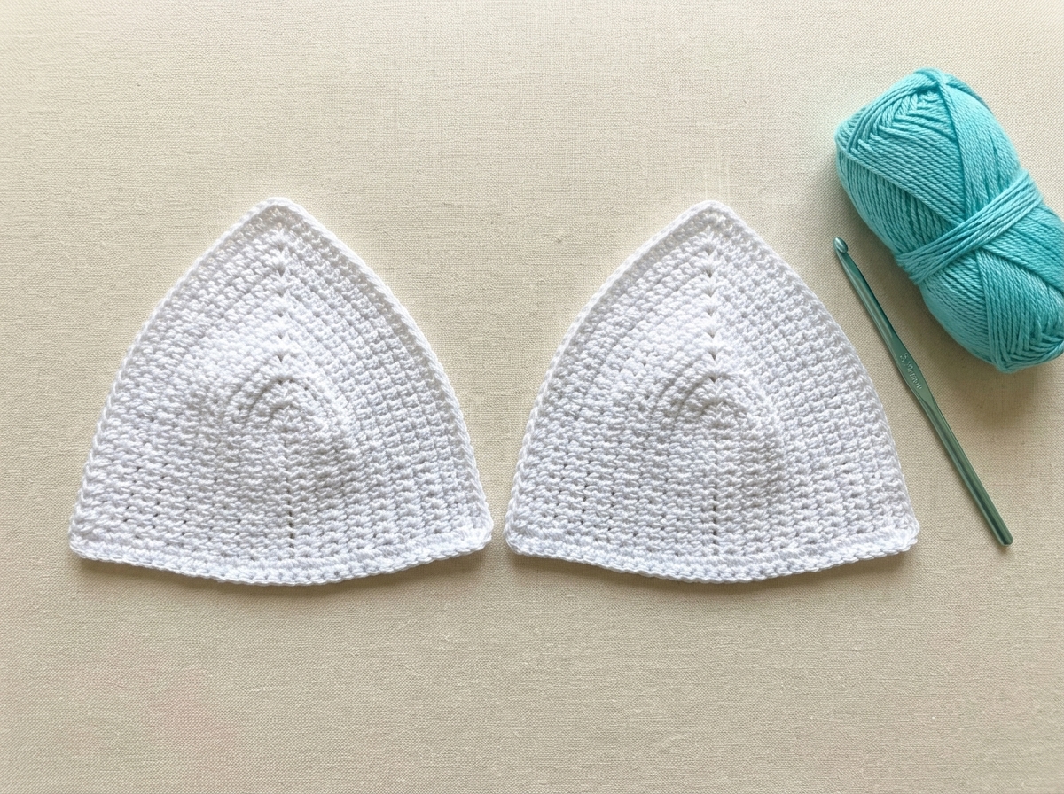 Two separate unjoined white single crochet triangle bikini cups laid flat next to aqua cotton yarn and a 3.75 mm hook