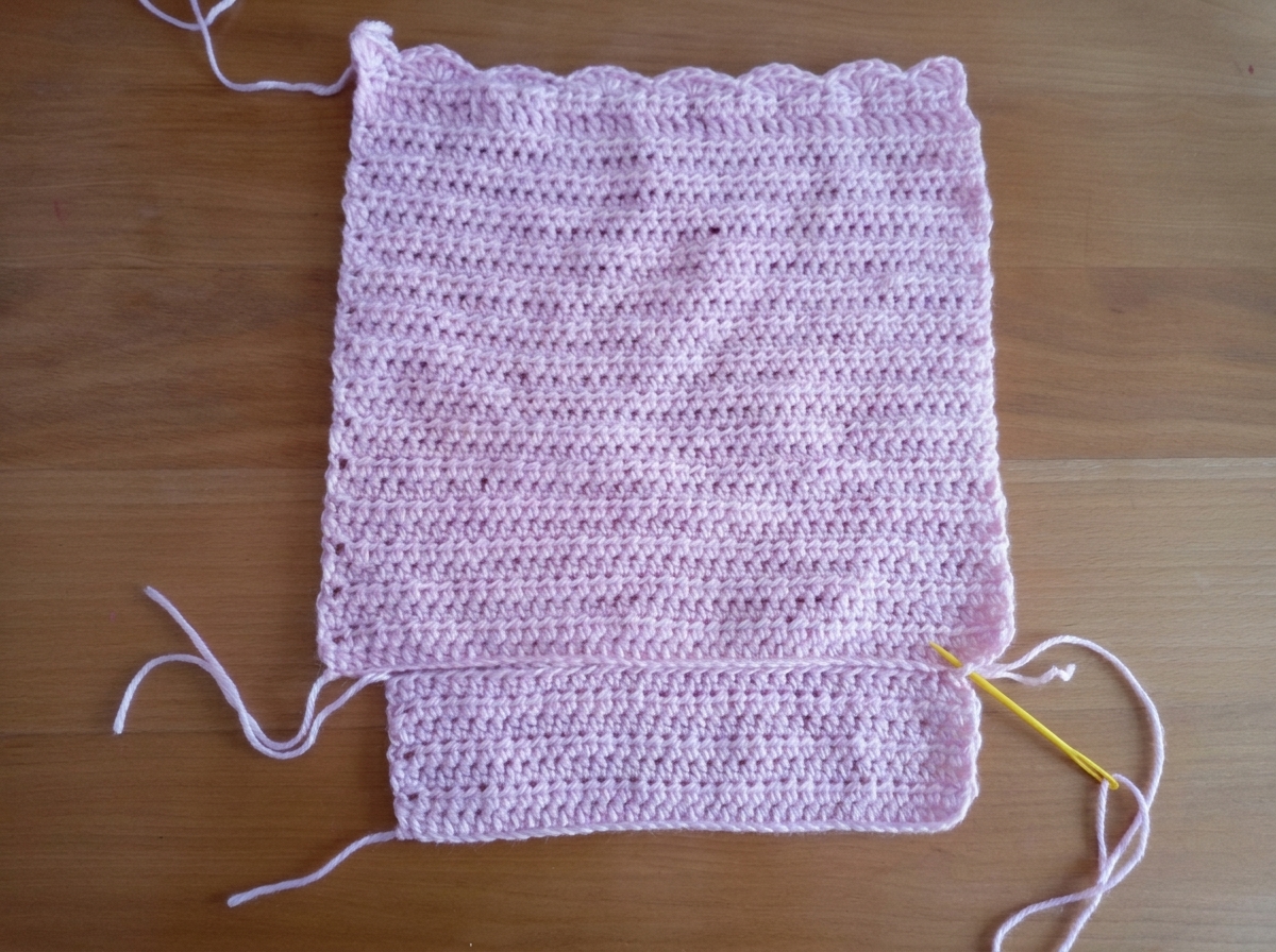 Step 2 of the crochet tote bag pattern sewing the bottom piece to the front panel with a yellow tapestry needle