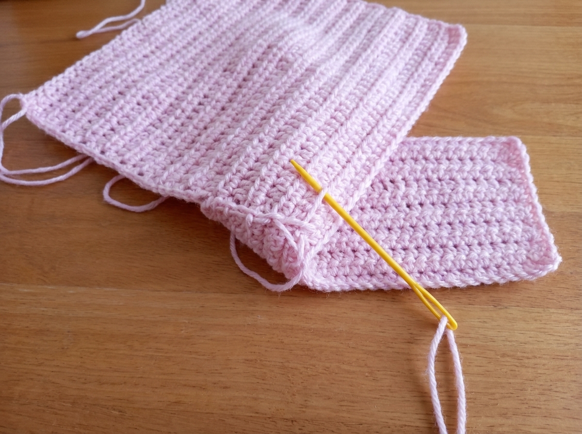 Step 3 of the crochet tote bag pattern wrapping and sewing the 3 corner stitches of the front panel around the short end of the bottom base