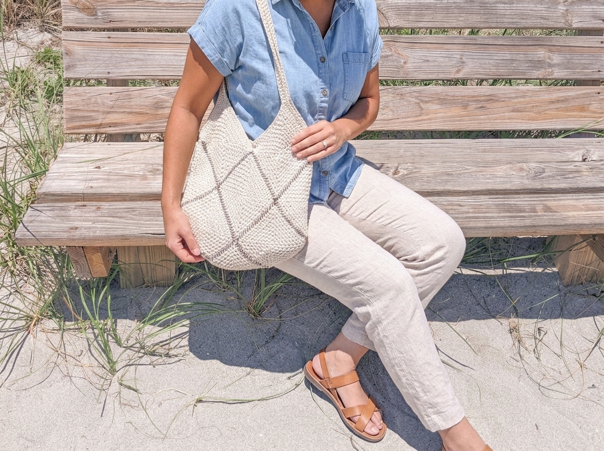 Model sitting on a wooden boardwalk bench with the cream crochet granny square bag beside her.