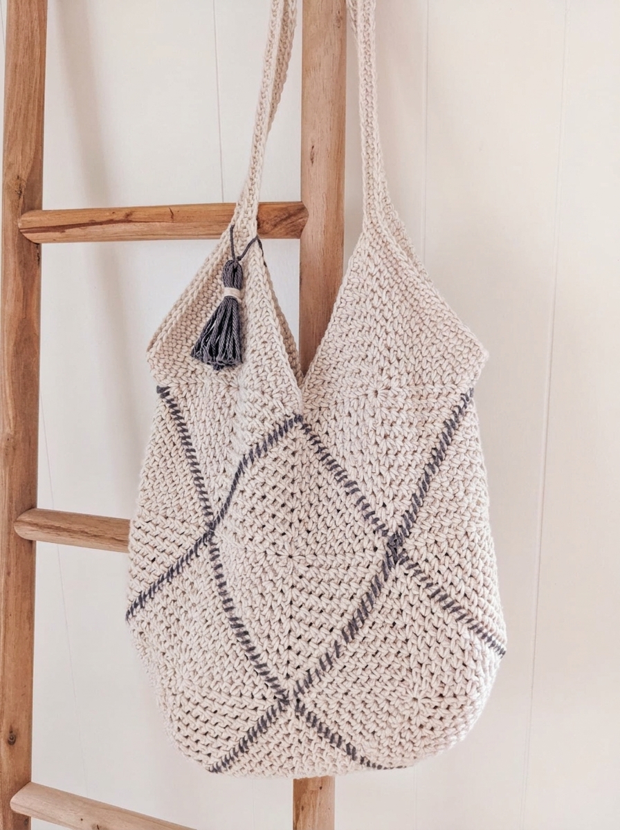 Close-up of the finished crochet granny square bag hanging on a wooden ladder showing the single crochet straps and charcoal tassel.