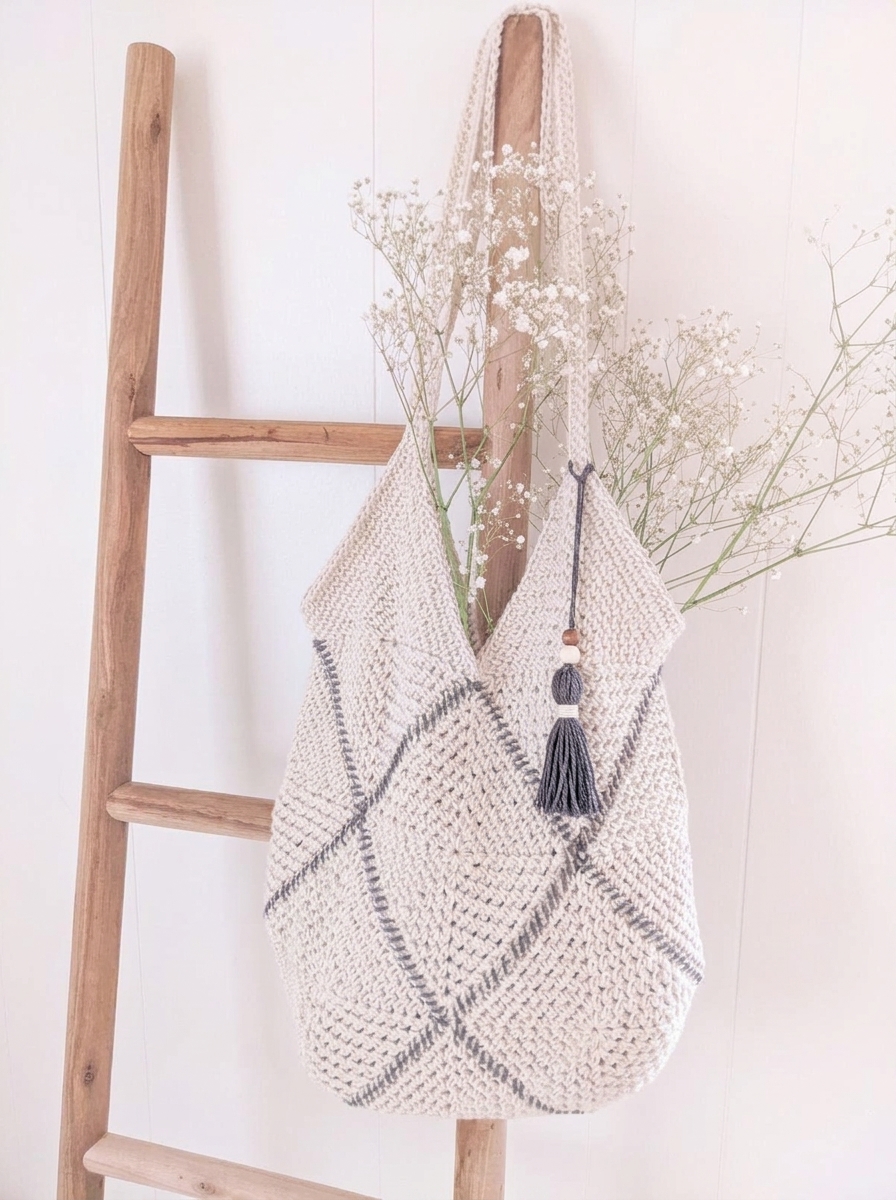 Crochet granny square bag in cream moss stitch with charcoal whipstitch seams hanging on a wooden ladder.