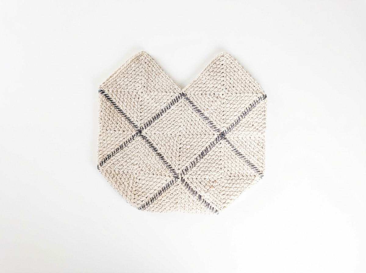 Fully seamed cream and charcoal crochet granny square bag body lying flat with two top peaks before adding straps.